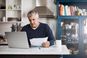 Photo d'un homme d'âge mûr en train de remplir des papiers alors qu'il travaille sur un ordinateur portable à la maison